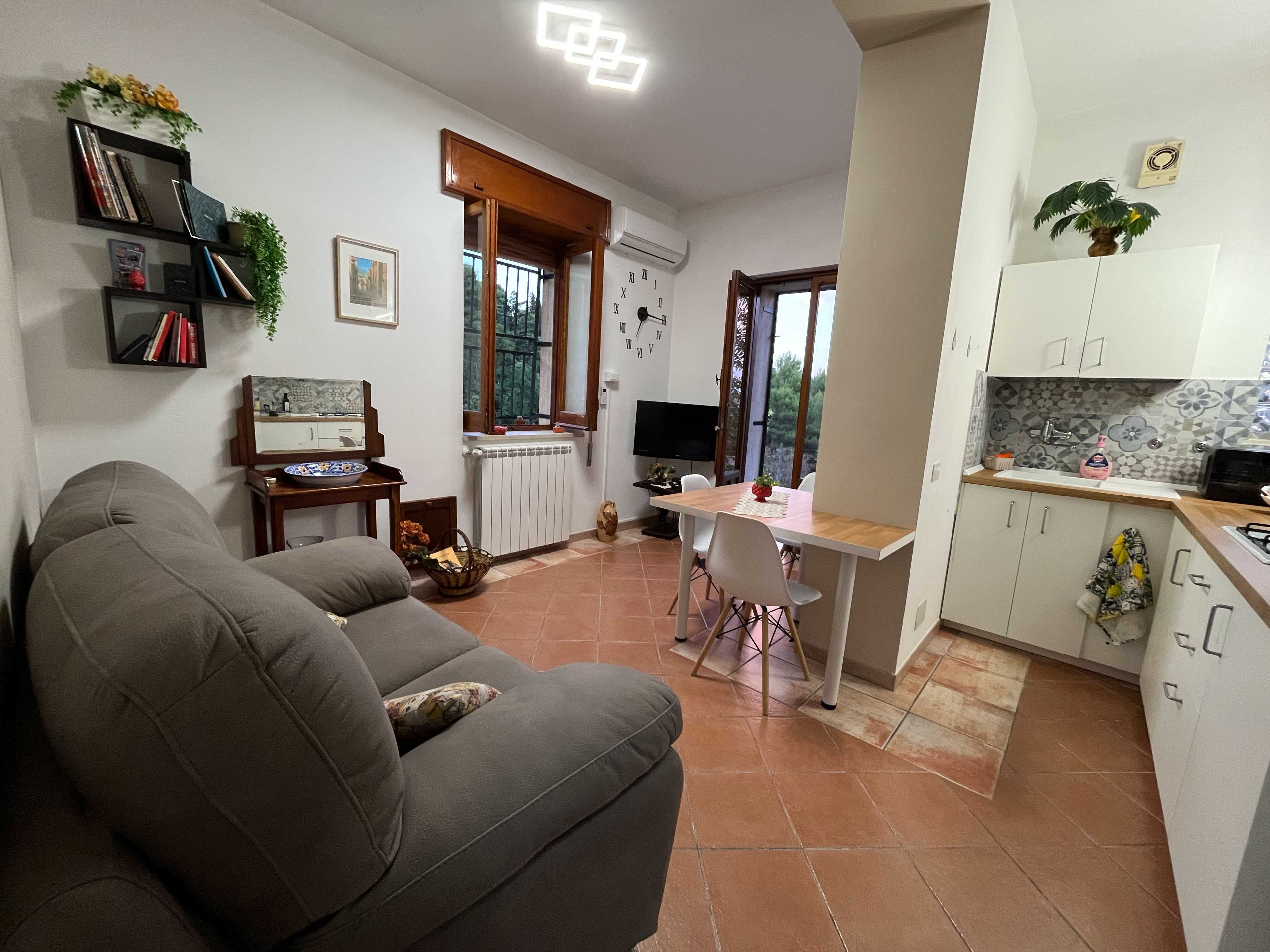 Una sala de estar con sofá, una mesa de comedor con sillas, un televisor y una cocina con armarios y microondas.