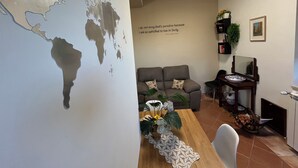 Un soggiorno con un murale raffigurante una mappa del mondo, un divano grigio, un tavolo da pranzo in legno con un runner in pizzo e una libreria con piante.