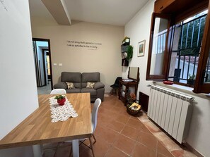 A cozy living area with a sofa, a dining table with a placemat, a radiator, and a window with a view. - Teresa's Holiday Home | Your Gateway to Western Sicily with private parking (Salemi)