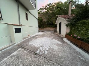 A paved courtyard with a small building, a metal fence, and a wooden planter with flowers. - Teresa's Holiday Home | Your Gateway to Western Sicily with private parking (Salemi)