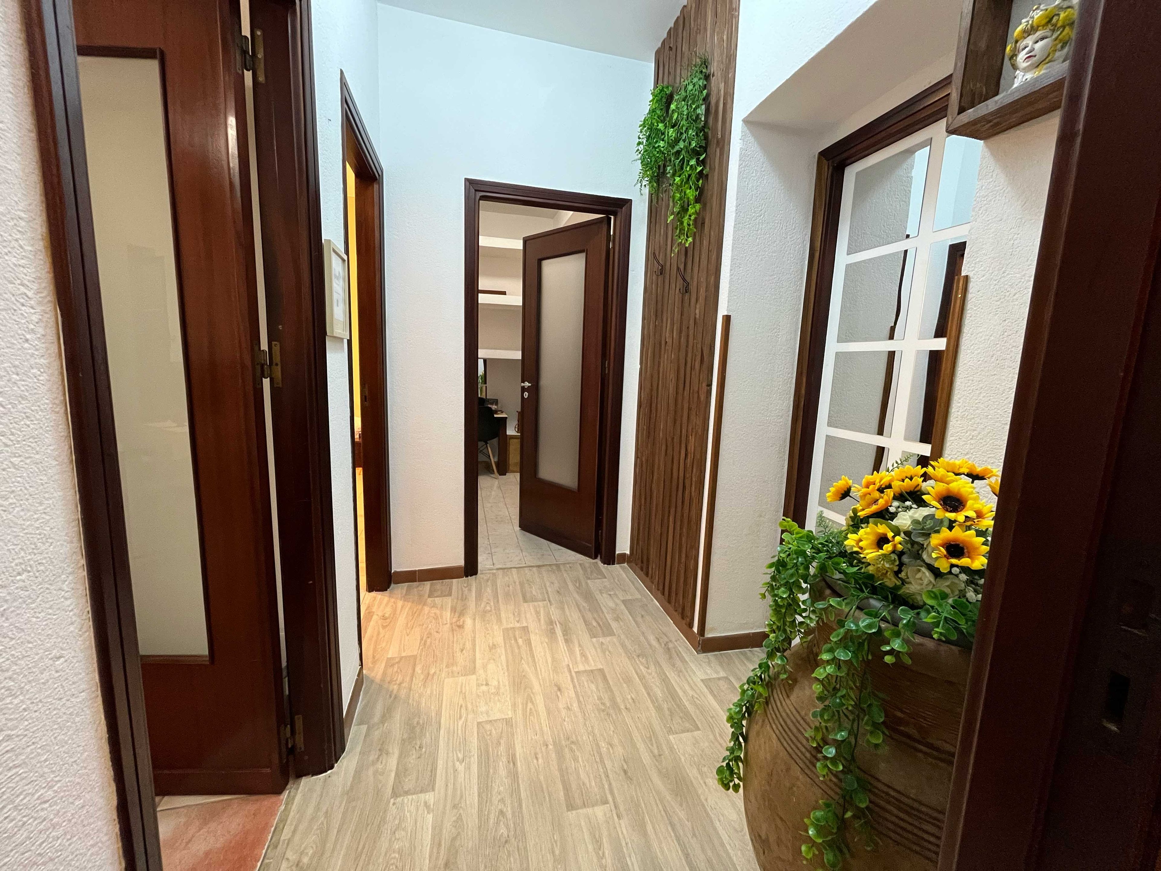 Un passadís amb portes de fusta, un paviment de fusta i una planta amb flors grogues.