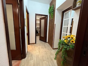 A hallway with wooden doors, a wooden floor, and a plant with yellow flowers. - Teresa's Holiday Home | Your Gateway to Western Sicily with private parking (Salemi)