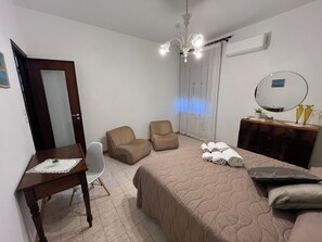 A bedroom with a bed, two chairs, a desk, a dresser, and a chandelier. - Teresa's Holiday Home | Your Gateway to Western Sicily with private parking (Salemi)