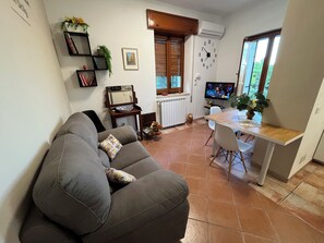 A living room with a sofa, a dining table, and a TV. - Teresa's Holiday Home | Your Gateway to Western Sicily with private parking (Salemi)