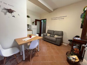 A dining area with a wooden table and white chairs, a grey sofa, and a wall with a quote. - Teresa's Holiday Home | Your Gateway to Western Sicily with private parking (Salemi)