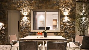 A stone-walled dining area with a table and chairs, a window with a view, and two wall-mounted lights. - Coel Luxury Suites S2 by RentalsPro (Nea Moudania)