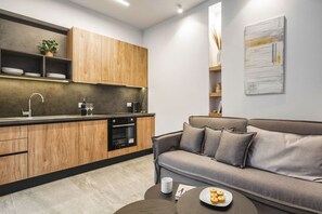 Eine moderne Küche mit Holzausbau und Backofen, ein graues Sofa mit Kissen sowie ein Couchtisch mit einem Teller Keksen.