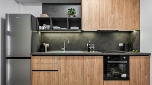A modern kitchen with a stainless steel refrigerator, wooden cabinets, a built-in oven, and a countertop with a sink and a coffee machine. - Coel Luxury Suites S2 by RentalsPro (Nea Moudania)