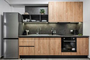 Eine moderne Küche mit Edelstahlkühlschrank, Holzschränken, einem Einbauofen und einer Arbeitsplatte mit Spüle und Kaffeemaschine.
