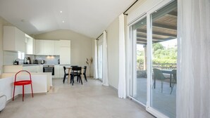 Eine moderne Küche mit weißen Schränken, ein Essbereich mit Tisch und Stühlen und eine Glastür, die auf eine Terrasse im Freien führt.