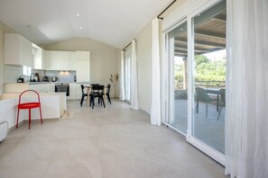 Eine moderne Küche mit weißen Schränken, ein Essbereich mit Tisch und Stühlen und eine Glastür, die auf eine Terrasse im Freien führt.