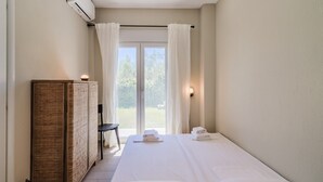 Ein Schlafzimmer mit einem Bett, einem Nachttisch, einem Kleiderschrank und Blick durch eine Glastür.