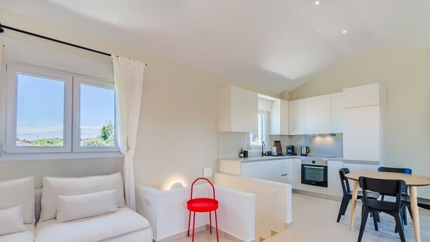 Ein modernes, minimalistisches Wohnzimmer mit einem weißen Sofa, einem roten Sessel und einem Essbereich mit Tisch und Stühlen.