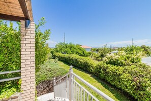 Ein Balkon mit Blick auf einen gepflegten Garten, eine Ziegelmauer und einen strahlend blauen Himmel.