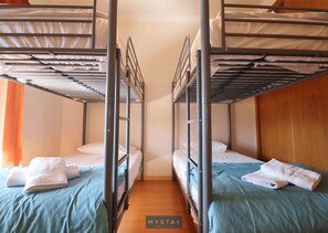 Ein Zimmer mit zwei Etagenbetten, jeweils mit Kissen und gefaltetem Handtuch. Das Zimmer hat Holzboden und eine schlichte Wand.