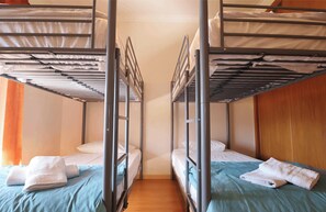 A room with two bunk beds, each with a pillow and a folded towel. The room has wooden flooring and a plain wall. - Vrbo Property (Alvite)