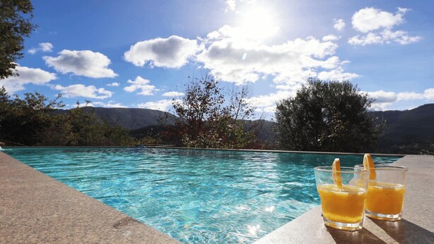 A swimming pool with clear water, two glasses of orange juice, and a mountainous landscape in the background. - MyStay - Casa do Carmo (Alvite)