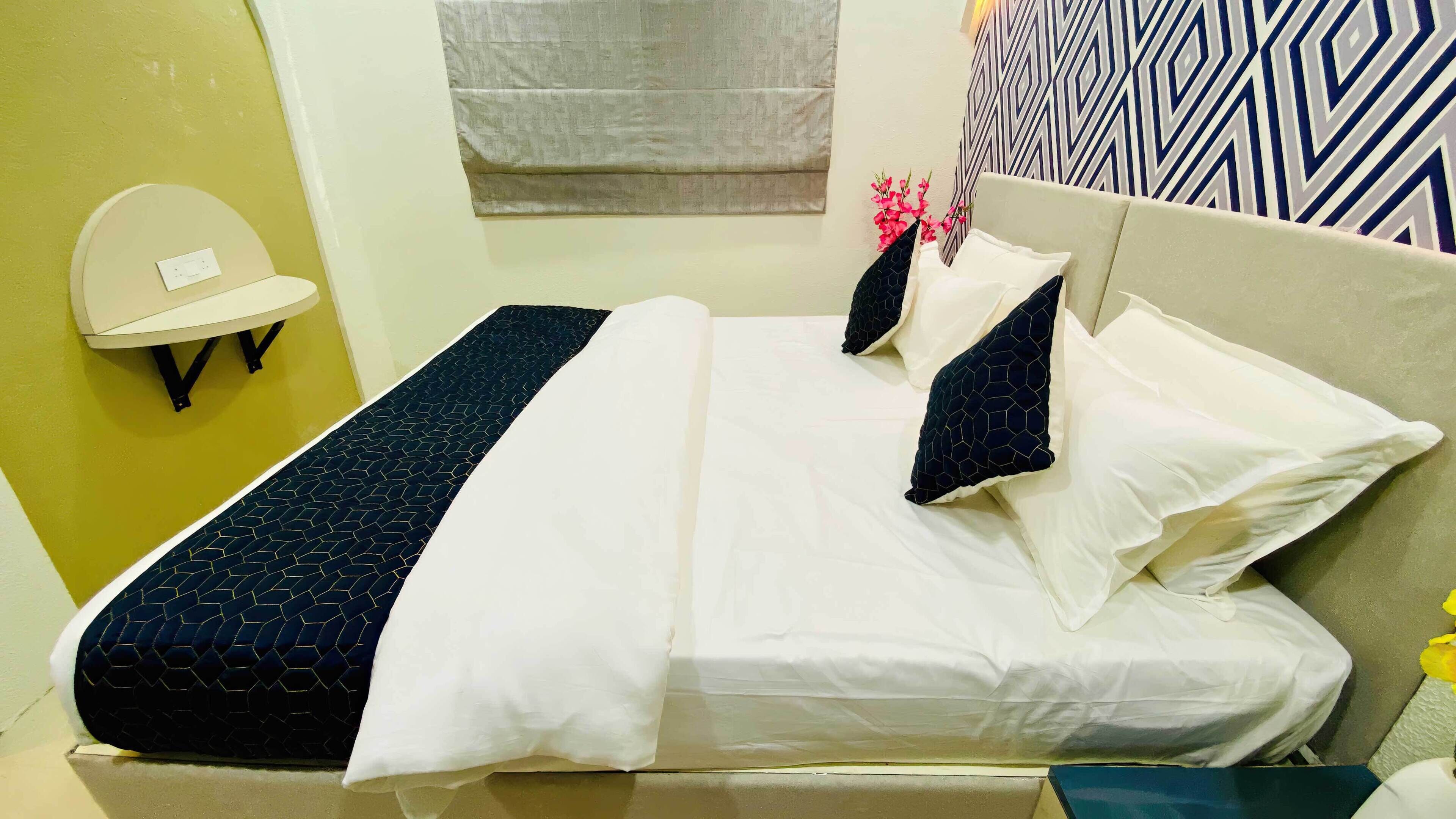 Un letto con lenzuola bianche e blu scuro, una lampada fissata al muro e una parete decorata.