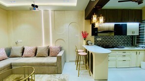 A modern living room with a sofa, a coffee table, and a kitchen area with a bar counter and stools.
