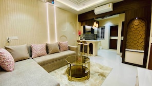 A modern living room with a sofa, a glass coffee table, and a kitchen area in the background. - Global Village BnB (Indore)