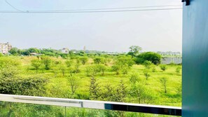 A view from a balcony overlooking a grassy field with trees, a distant building, and a clear sky. - Global Village BnB (Indore)