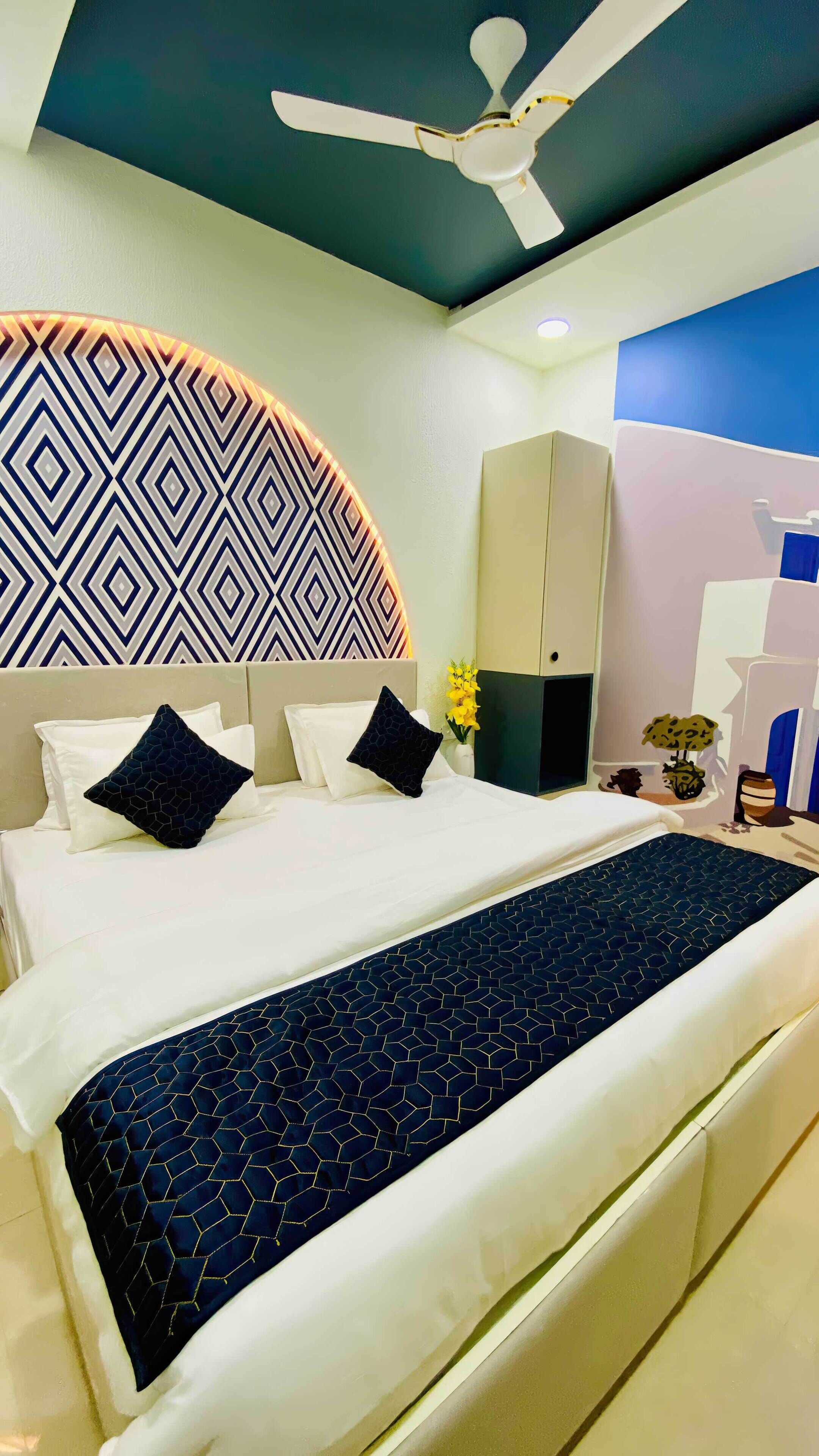 A hotel room with a bed, a ceiling fan, a wardrobe, and a decorative wall.