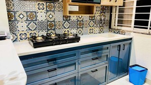 A kitchen with a gas stove, blue cabinets, and patterned backsplash. - Global Village BnB (Indore)