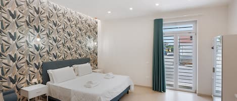 A hotel room with a bed, a nightstand, a dresser, and a view of the street through a door.