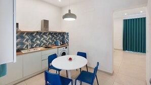 Una cocina funcional con lavadora, una mesa de comedor con sillas e iluminación colgante.