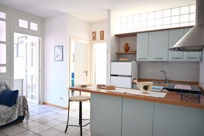 A kitchen with a central island, a refrigerator, and a sink. There is a chair and a sofa in the adjacent living area. - S376 - Sirolo, three-room apartment with a furnished balcony and parking space. (Sirolo)