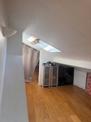 Ein Zimmer mit schrägem Dach, einem Oberlicht, einem Kleiderschrank und einem gemusterten Kühlschrank.