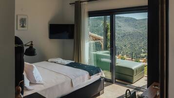 A bedroom with a bed, a TV, a desk, a chair, a window, and a view of a mountainous landscape.