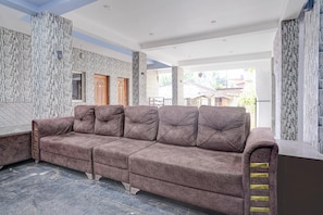 A modern living room with a sectional sofa, stone-patterned walls, and a view of the outside. - Family Rooms With Twin King bed Ravai (Calangute)
