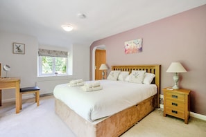 A bedroom with a large bed, bedside lamps, a wooden nightstand, a desk, and a window with a view of greenery. - Waters Edges cottage up to 12 in the beautiful peaceful Lake District location. (Selside)