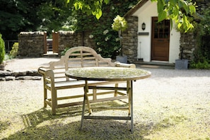 A wooden bench and table set on a gravel surface with a stone wall and a building in the background. - Waters Edges cottage up to 12 in the beautiful peaceful Lake District location. (Selside)