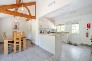 A kitchen with white cabinets, a wooden dining table, and a large island. - Waters Edges cottage up to 12 in the beautiful peaceful Lake District location. (Selside)