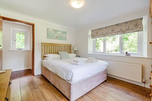 A bedroom with a wooden bed, a window with a view of greenery, and a radiator. - Waters Edges cottage up to 12 in the beautiful peaceful Lake District location. (Selside)