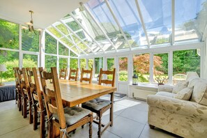 A conservatory with a glass roof, wooden dining table, chairs, and a sofa. - Waters Edges cottage up to 12 in the beautiful peaceful Lake District location. (Selside)
