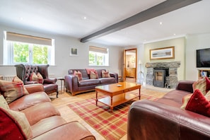 A spacious living room with leather sofas, a wooden coffee table, and a stone fireplace. - Waters Edges cottage up to 12 in the beautiful peaceful Lake District location. (Selside)