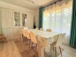 En matplats med ett bord, stolar, ett skåp med glasdörrar och ett fönster med gardiner.