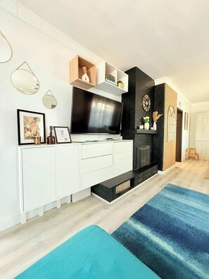 Un salon moderne avec un téléviseur à écran plat, des meubles blancs, une cheminée noire et un tapis bleu.