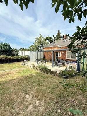 En bostadsfastighet med ett hus i tegel, en täckt uteplats och en gräsmatta.