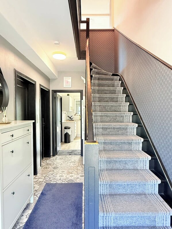 Un escalier avec une rampe menant à un palier, une commode blanche avec des tiroirs et un tapis à motifs.
