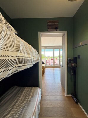 Une pièce avec un lit, une porte donnant sur un balcon et un aspirateur fixé au mur.