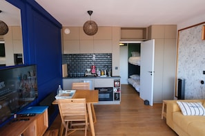 A compact living space with a kitchenette, a dining area, a seating area, and a television. - Arcachon centre - Studio Cabine superbe vue mer - accès plage (Arcachon)