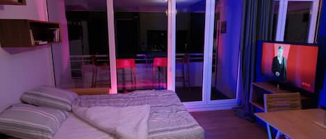 Una habitación con cama, televisor, mesa y puerta corrediza de vidrio que da a un espacio exterior.