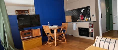 Un espacio habitable compacto con kitchenette, zona de comedor con mesa y sillas, sofá y televisor.