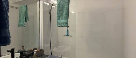 A modern bathroom with a white sink, black marble countertop, a glass-enclosed shower, and a white bathtub.
