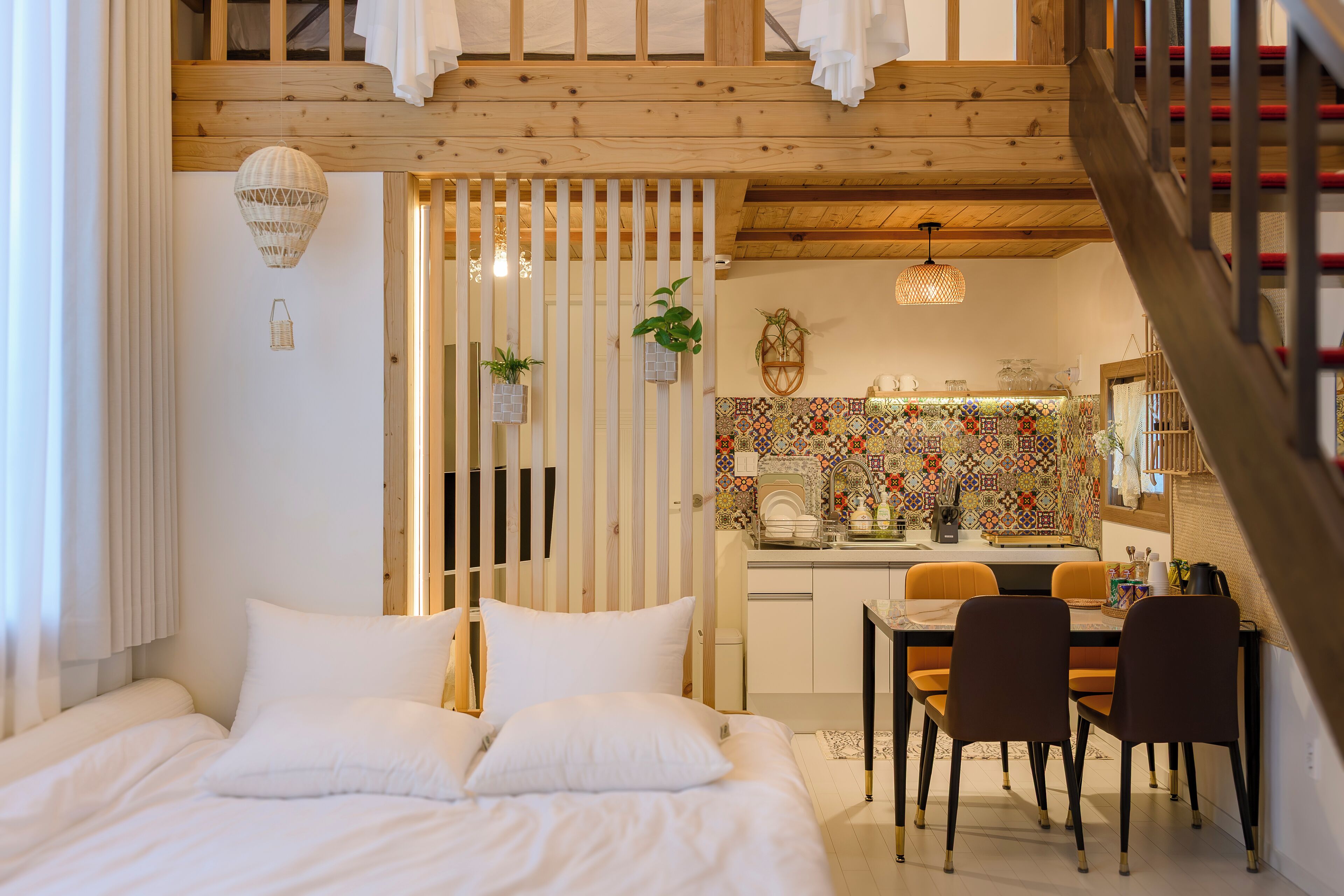 Ein Schlafzimmer mit einem Bett, einem Essbereich mit Stühlen, einer Küche mit farbenfroher Spritzschutzleiste und einer Holzbalkendecke.