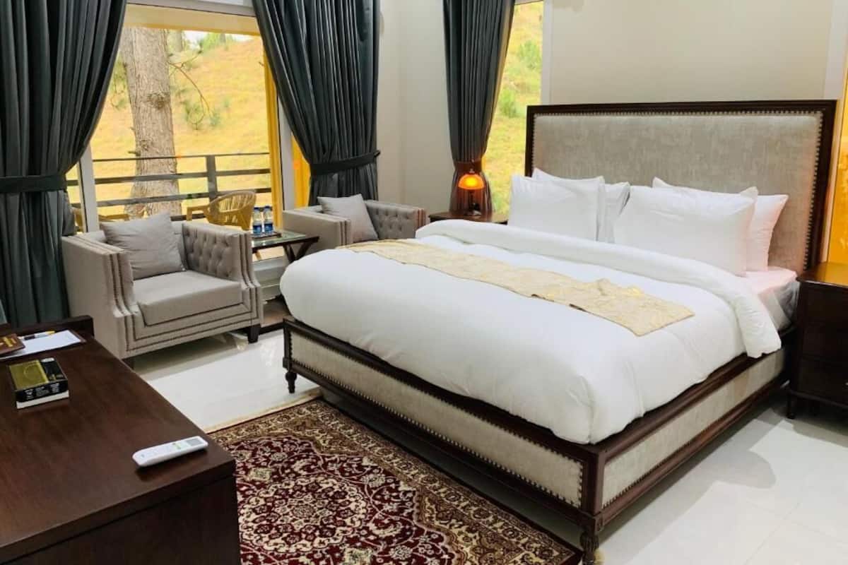 Un dormitorio amplio con una cama grande, una zona de estar con una silla y una mesita, y vistas al exterior a través de amplios ventanales.